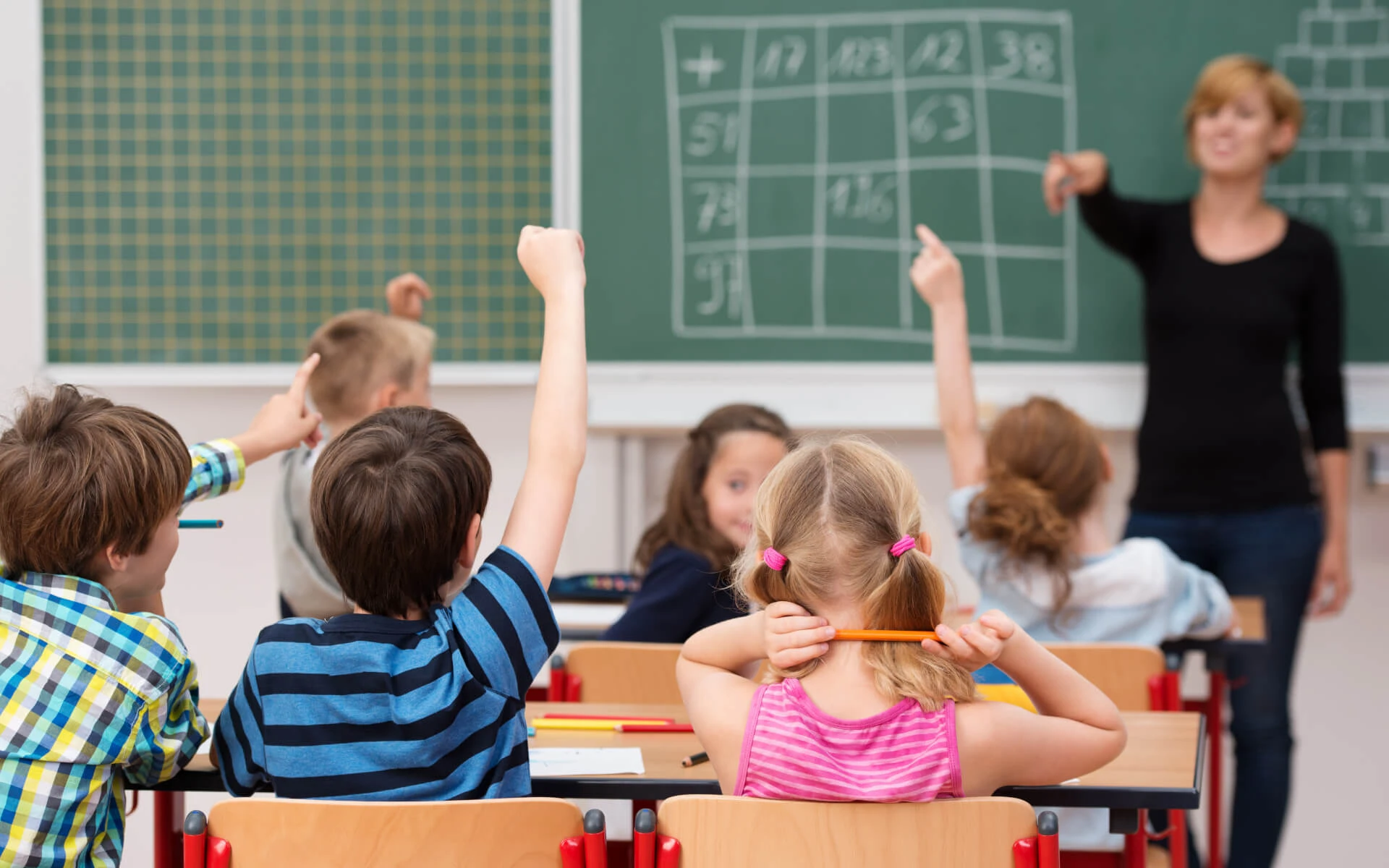 Sechs Kinder sitzen im Matheunterricht und lösen mit der Lehrerin Aufgaben an der Tafel.