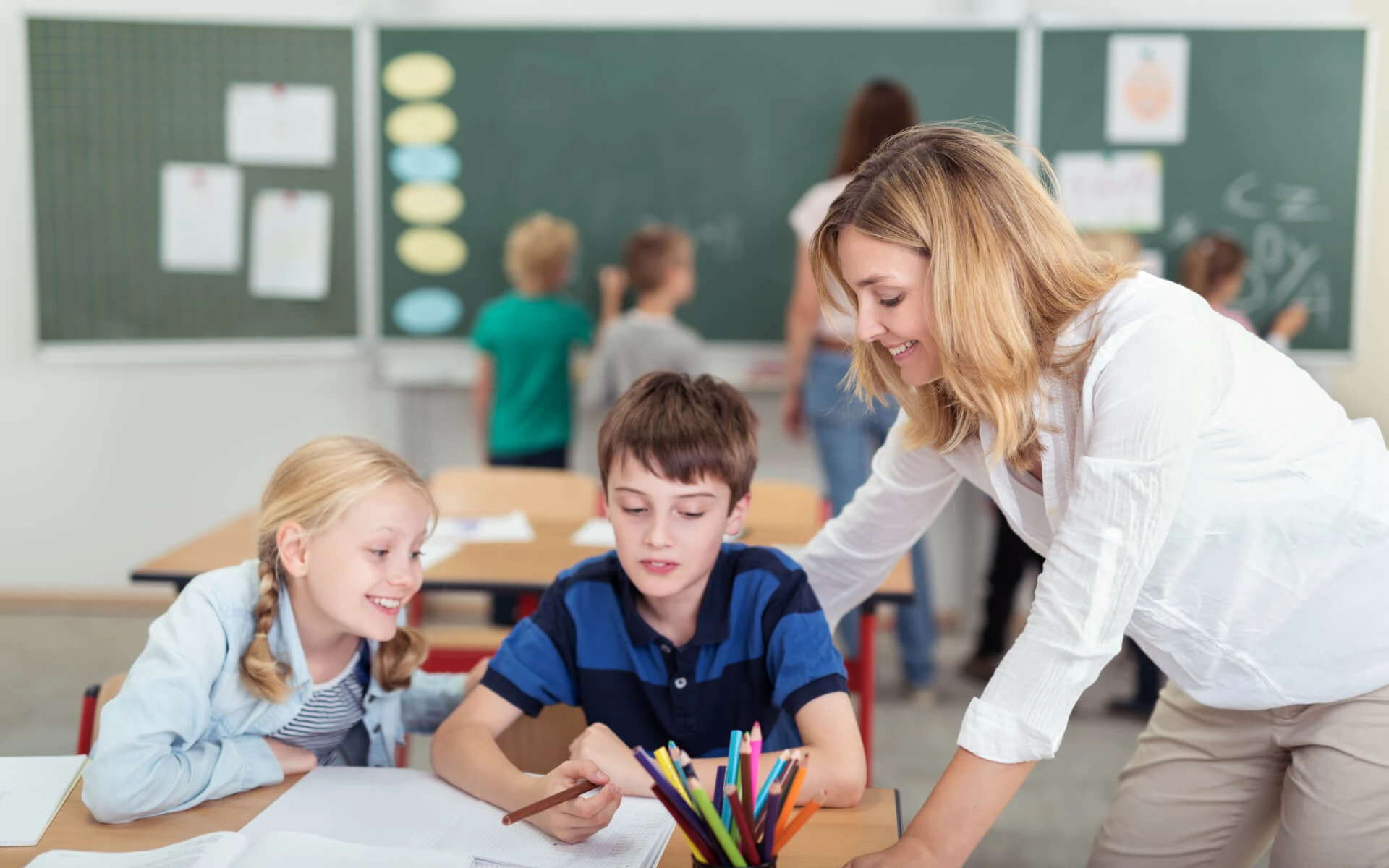 Eine Schulbegleiterin hilft zwei Kindern im Klassenraum.