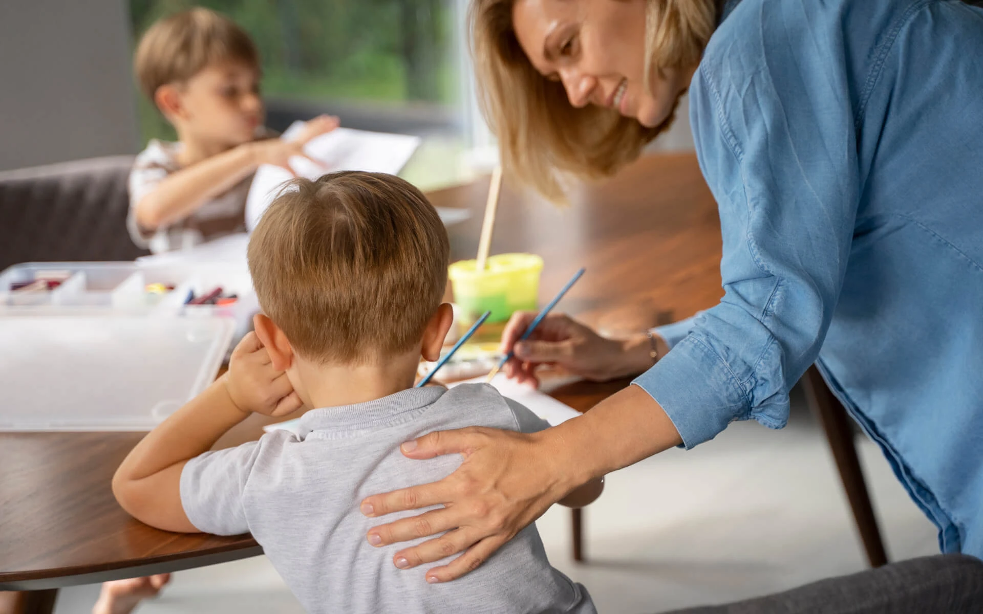 Eine Schulbegleiterin hilft einem kleinen Jungen etwas zu malen.